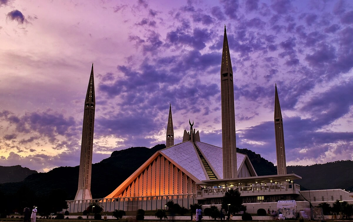 Faisal Mosque in Islamabad at sunset with glowing lights, tall minarets, and scenic mountain backdrop, a key landmark for travelers in 2026.